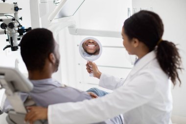 Siyahi adam aynaya bakıyor, dişlerini kontrol ediyor.