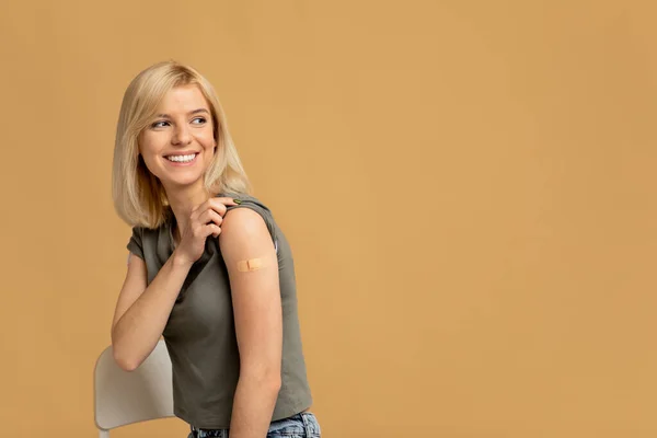 Covid-19 вакцинована щаслива леді, що показує руку після ін'єкцій і дивиться на простір копіювання на студійному фоні — стокове фото