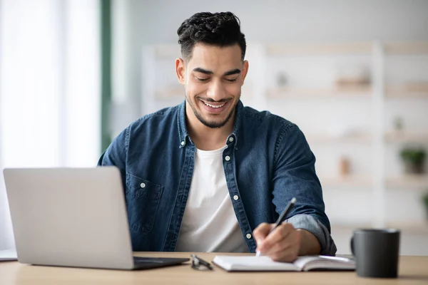 Fröhlicher Araber macht sich Notizen bei der Arbeit mit Laptop — Stockfoto