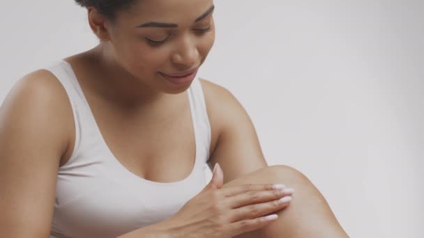Jeune femme africaine américaine attrayante appliquant de la crème pour le corps sur ses jambes lisses et souriant, bénéficiant de procédures de beauté — Video