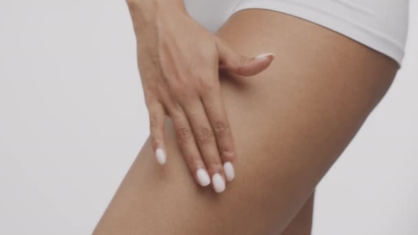 Primo piano di donna afroamericana irriconoscibile che applica crema lifting cutaneo su fianchi, sfondo bianco, rallentatore — Video Stock