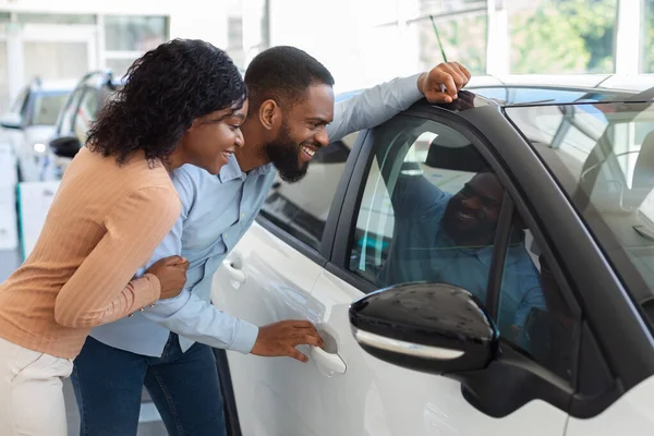 Carro novo. Cônjuges negros excitados olhando para o novo automóvel no escritório de concessionárias — Fotografia de Stock