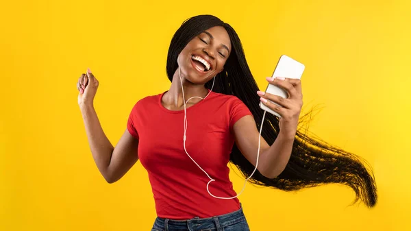 Afrikaanse vrouw dansen luisteren naar muziek dragen koptelefoon, gele achtergrond — Stockfoto