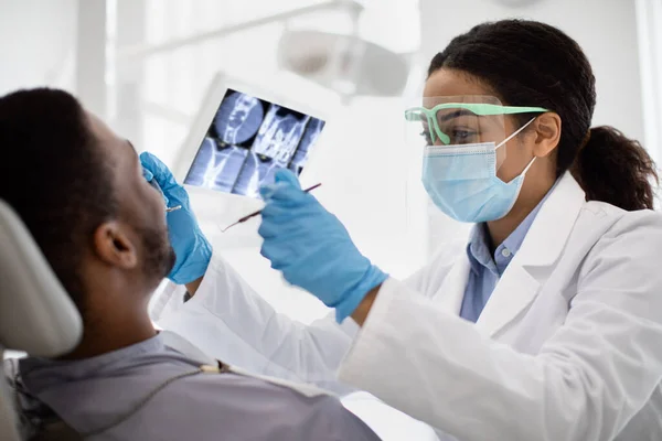 Dentista negro dama examinando dientes de paciente masculino con herramientas dentales estériles —  Fotos de Stock