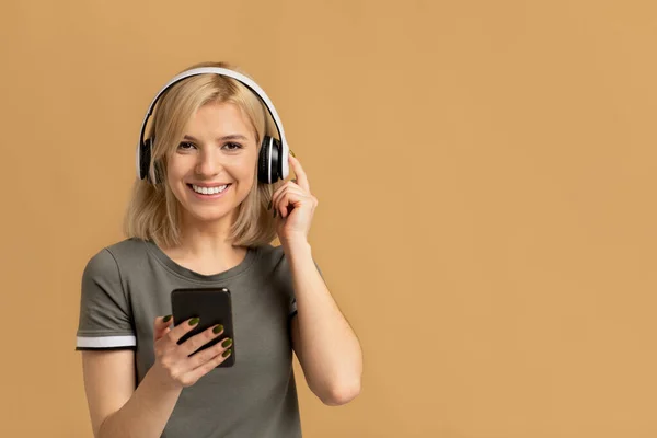 Retrato de senhora emocional ouvindo música em fone de ouvido sem fio, de pé isolado no fundo do estúdio pêssego — Fotografia de Stock