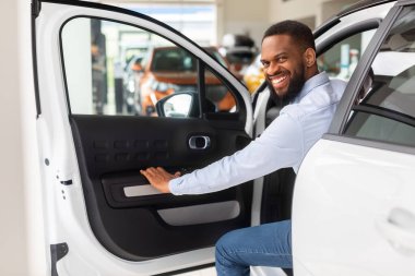 Yeni arabasında poz veren ve kameraya gülümseyen mutlu siyah adam.