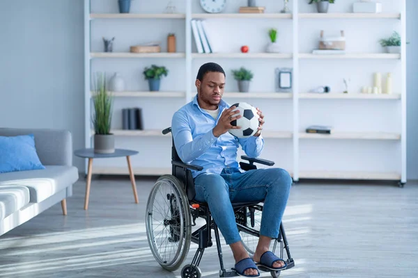 Depressieve gehandicapte zwarte man in rolstoel kijkt naar voetbal met verdriet, gestrest over letsel of handicap — Stockfoto