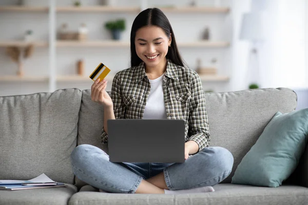 Alegre asiático mujer usando laptop y tarjeta de crédito en casa — Foto de Stock