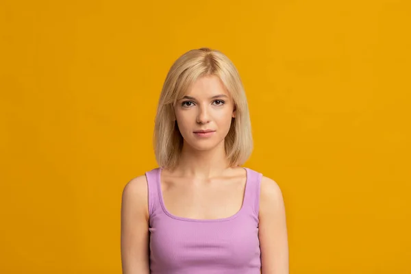 Retrato de cerca de una joven con expresión seria en su rostro posando sobre un fondo de estudio amarillo, espacio para copiar — Foto de Stock