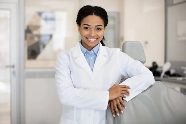 Portré fekete női fogorvos fehér kabátban pózol a klinika belsejében — Stock Fotó