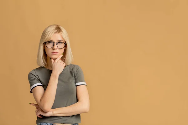 Porträtt av pensiv dam i glasögon vidröra haka och tänka på fråga över persika bakgrund, fritt utrymme — Stockfoto
