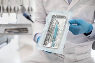 Tanımlanamayan Diş Hekimi Üniformalı Doktor diş aletleriyle mühürlü sterilizasyon kesesini gösteriyor.