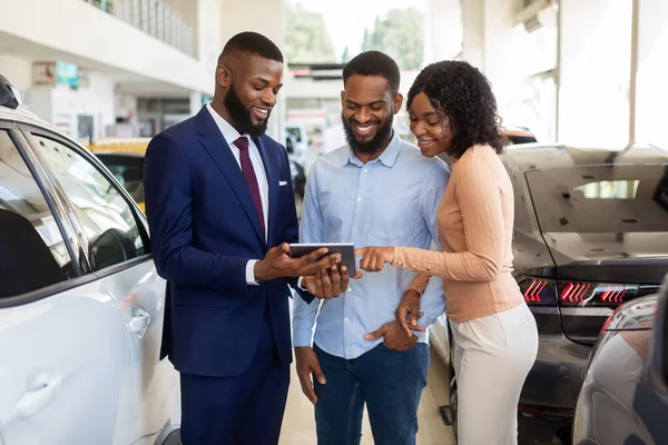 Dealership Center Manager Showing Vehicle Characteristics On Digital Tablet To Black Couple — Stock Photo, Image