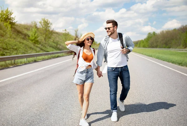 Full längd av unga par promenader längs vägen, hålla händer, fånga rida, väntar på bil, kopiera utrymme — Stockfoto