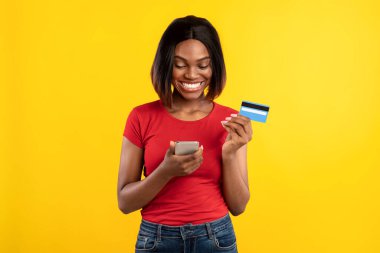 Siyah Kadın Telefon ve Kredi Kartını Sarı Arkaplanda Kullanıyor