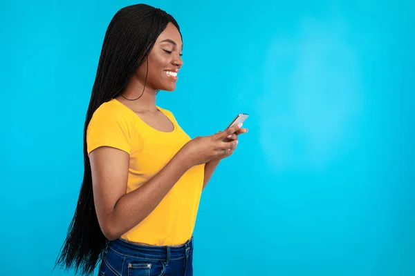 Vista lateral de la mujer negra feliz usando el teléfono sobre fondo azul — Foto de Stock