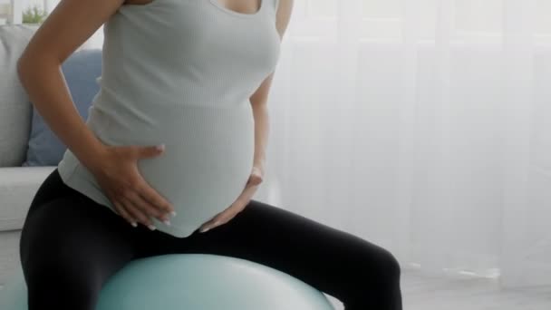 Mujer embarazada haciendo ejercicios en la pelota de fitness en casa, disparo de primer plano — Vídeo de stock