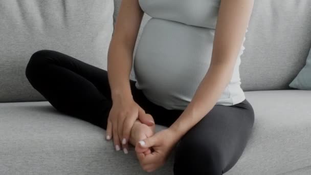 Беременная женщина массирует распухшую ногу, сидя дома на диване — стоковое видео