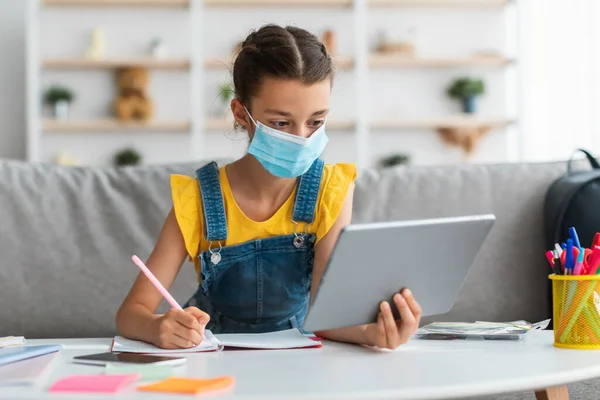 Μαθήτρια με ιατρική μάσκα που σπουδάζει στο σπίτι με ψηφιακή ταμπλέτα — Φωτογραφία Αρχείου