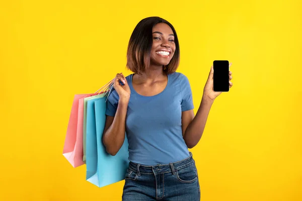 Donna africana che mostra lo schermo dello smartphone in posa con borse shopper, Studio — Foto Stock