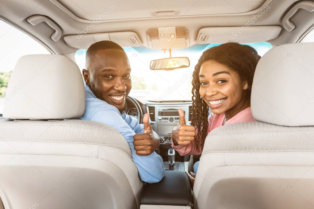 Happy black couple sitting in auto gesturing thumbs up