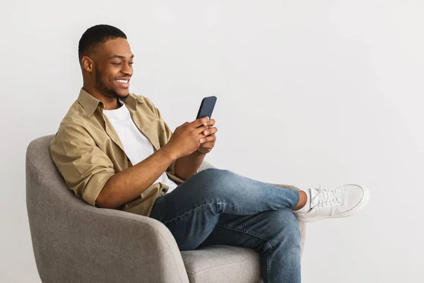 Hombre afroamericano feliz usando Smartphone sentado sobre fondo gris —  Fotos de Stock