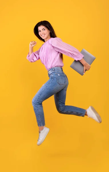 Щаслива вірменка стрибає або біжить з портативним комп'ютером в руці, розважаючись на жовтому студійному фоні — стокове фото