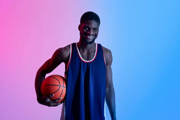 Happy young black basketball player holding ball, smile at camera in neon light — Stok Foto