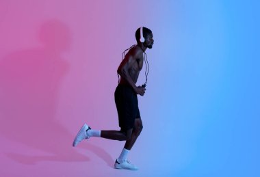 Uzun boylu, göğsü çıplak, kulaklık takan, ip atlayan, neon ışıkta koşan, kenar görüşlü, atletik bir zenci.