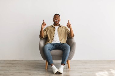 Siyahi adam parmaklarını yukarı kaldırıyor Gri duvarın üzerinde oturuyor