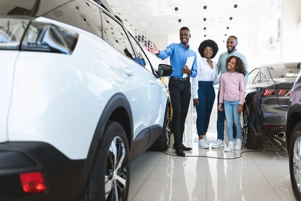 Otomobil satıcısı araba galerisindeki genç siyahi aileye lüks araba gösteriyor. — Stok fotoğraf