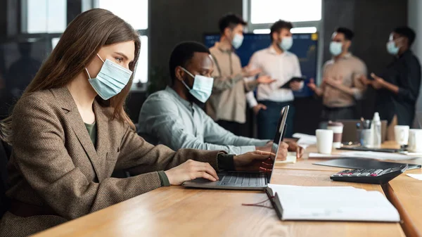 Collega 's die werken aan een project met gezichtsmaskers die gebruik maken van technologie — Stockfoto