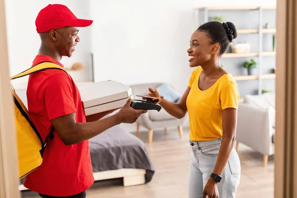 Afrikaanse vrouw betalen koerier voor pizza met mobiele telefoon binnen — Stockfoto