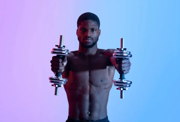 Porträt eines ernsthaften afroamerikanischen Power-Hebers mit nacktem Oberkörper, der mit Hanteln im Neonlicht trainiert — Stockfoto