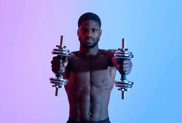 Retrato de levantador de energia afro-americano sério com tronco nu trabalhando com halteres em luz de néon — Fotografia de Stock