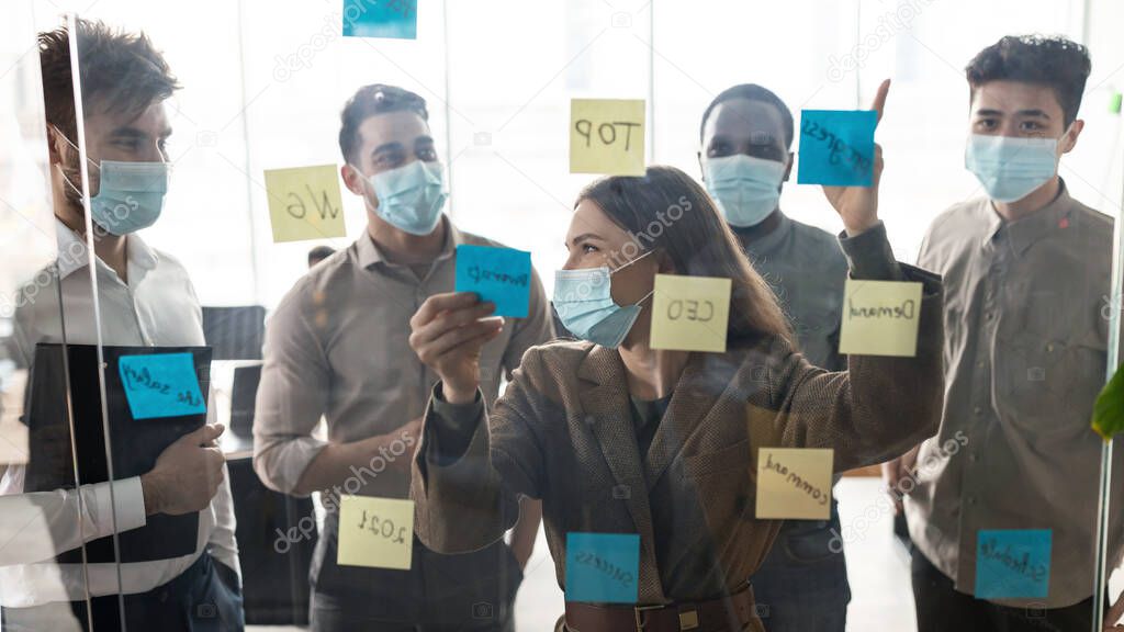 Businesspeople in disposable masks brainstorming using post-it notes on wall