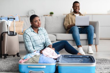 Kocası evde dizüstü bilgisayar kullanırken Afrikalı Eş Seyahat Bavulu Topluyor
