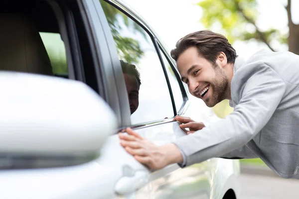 Mann umarmt neues Auto, von dem er träumt, steht im Autohaus neben weißem Automobil, will es kaufen — Stockfoto