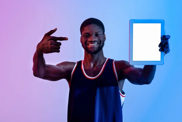 Pozytywny czarny sportowiec pokazujący tablet z pustym ekranem w neonowym świetle, makietą do projektowania aplikacji lub strony internetowej — Zdjęcie stockowe