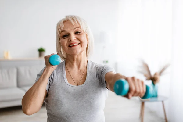 Mujer madura alegre haciendo ejercicio en casa con dos pesas — Foto de Stock