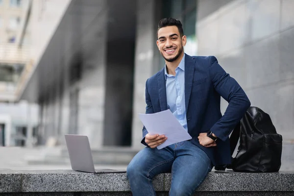Empresario árabe guapo sentado junto al edificio de oficinas con computadora portátil — Foto de Stock