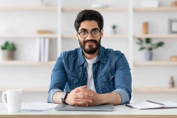 Портрет уверенного араба-предпринимателя, сидящего за столом в домашнем офисе и улыбающегося в камеру, копирующего пространство — стоковое фото