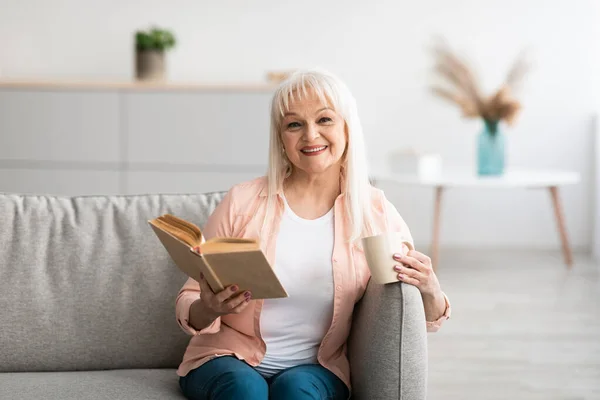 Boldog idősebb nő, amelynek pihenés otthon, olvasás könyv — Stock Fotó