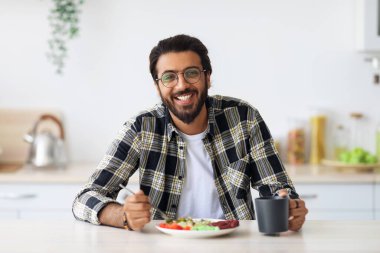 Neşeli orta doğulu genç adam evde sağlıklı bir öğle yemeğinin tadını çıkarıyor.