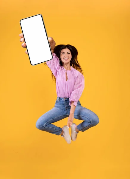 Mobil alkalmazás hirdetése. Izgalmas örmény hölgy ugrás és mutatja okostelefon üres képernyőn — Stock Fotó