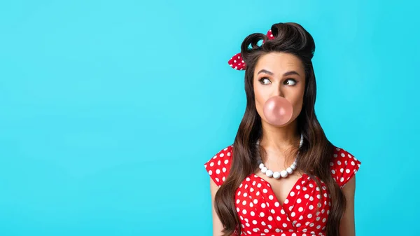 Playful pinup woman in retro style wear blowing bubble, chewing gum, looking at empty space on blue background — Stock Photo, Image