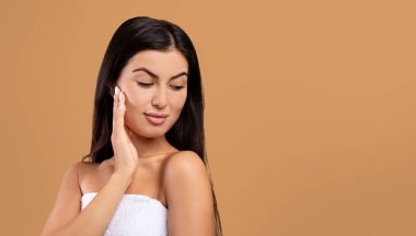 Spa yüz konsepti. Güzel Ermeni kadın yumuşak tenine dokunuyor, kahverengi arkaplanda fotokopi uzayıyla poz veriyor.