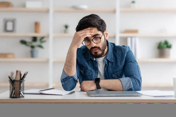 Stressiger Job. Gestresster Araber, der am Arbeitsplatz Probleme mit dem Kopf hat, sitzt zu Hause im Büro mit geschlossenem Laptop — Stockfoto