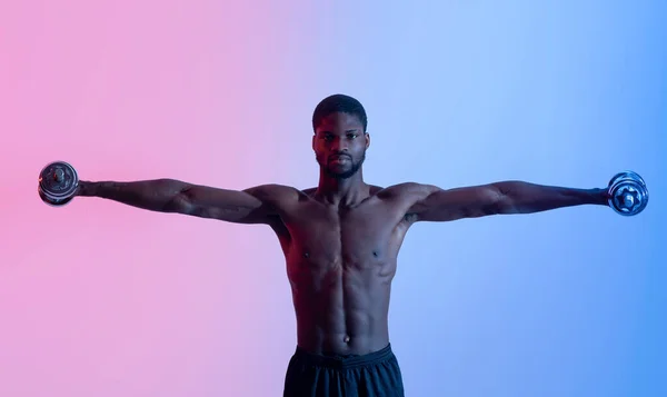 Forte jovem homem negro com torso nu levantando halteres em luz de néon, panorama — Fotografia de Stock