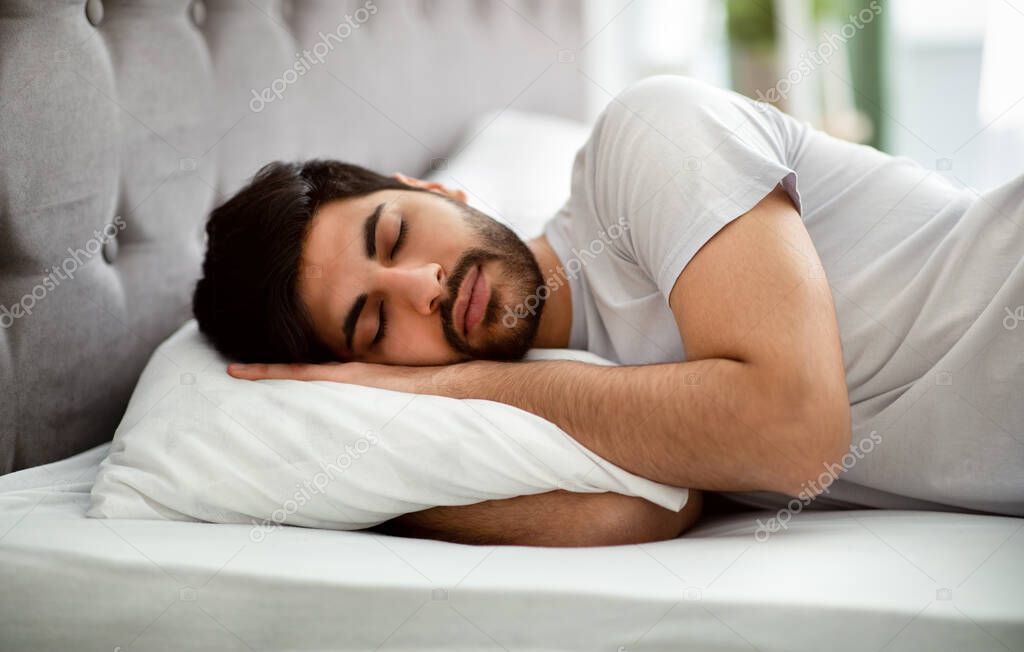 Comfortable sleep. Millennial arab man sleeping peacefully and see sweet dreams, lying in comfy bed and hugging pillow